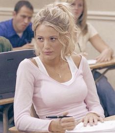 a woman sitting at a desk with a pen in her hand and two other people behind her