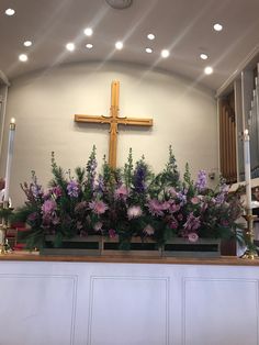 the flowers are in front of the cross on the wall above the alter, with people sitting at the pews behind them