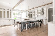 a large kitchen with white cabinets and counter tops, along with bar stools that match the hardwood flooring