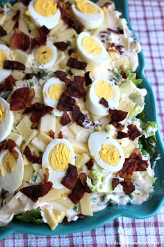 a salad with eggs and bacon in it on a blue platter sitting on a checkered table cloth