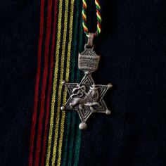 a star of david pendant on a multi - colored striped shirt with a red, green, yellow and blue ribbon