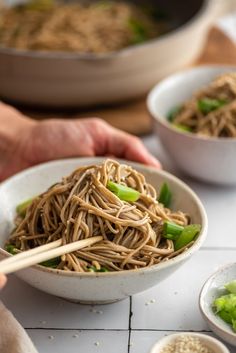 someone is holding chopsticks over a bowl of noodles and vegtables