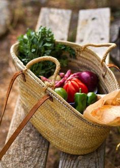 a basket filled with vegetables sitting on top of a wooden bench next to a bag