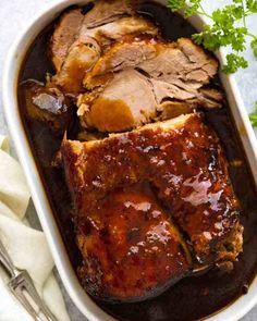 meat and vegetables in a casserole dish with garnish on the side