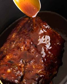 someone pouring sauce on top of a piece of meat in a slow - cooker