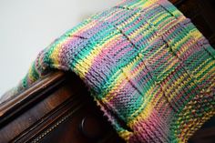 a multicolored knitted blanket sitting on top of a wooden dresser