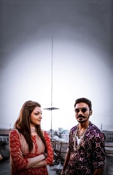 a man and woman standing next to each other in front of a tall building with a sky background