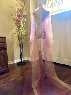 a dress on display in front of a stained glass window and vase with flowers behind it