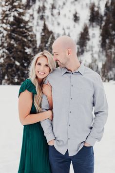 a man and woman standing in the snow with their arms around each other, smiling