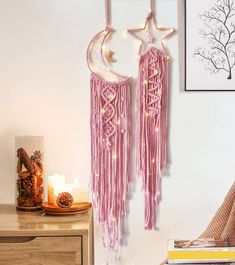 two pink dream catchers hanging on the wall next to a night stand with candles