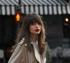 a woman walking down the street wearing a trench coat and red lipstick on her lips