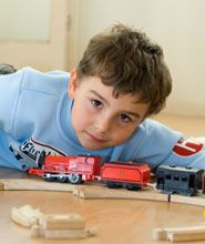 a young boy laying on the floor next to a toy train set with cars and tracks