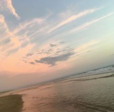 a person walking on the beach with a surfboard in their hand and clouds in the sky