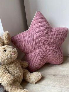 a teddy bear sitting next to a crocheted star pillow on the floor in front of a wall