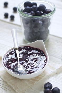 a bowl of blueberries with a spoon in it next to a jar of blueberries