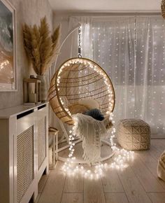 a hanging chair with lights around it in a room that has white curtains and wooden floors