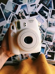 a person holding up a white camera in front of pictures on the wall behind them