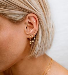 a woman with blonde hair wearing two gold ear cuffs and an earring that has three small bars attached to it