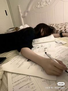 a woman laying on top of a bed with lots of papers and writing utensils