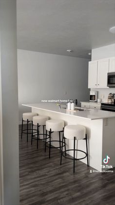 an empty kitchen with white counter tops and stools