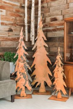 three wooden christmas trees in front of a wood paneled wall with white birch trees