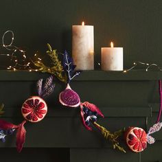 two candles are sitting on top of a mantle decorated with pomegranates