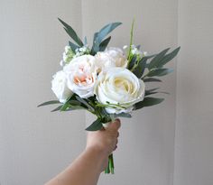 a person holding a bouquet of white and pink flowers with green leaves in their hand