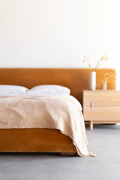 a bed sitting next to a wooden dresser with two vases on top of it