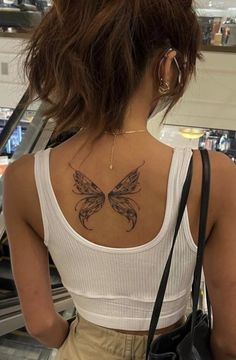 a woman with a butterfly tattoo on her back is looking down an escalator