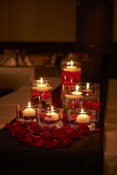 candles are arranged in glass vases on a table with red roses and petals around them