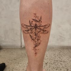 a woman's leg with a tattoo on it that has a dragonfly and flowers