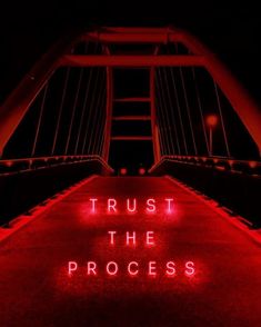 the words trust the process are lit up in red on a bridge at night time