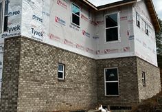 a house under construction with brick walls and windows in the front yard, next to a white fire hydrant