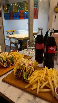 two sandwiches and french fries on a cutting board next to sodas in a restaurant