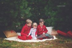 two young children sitting on a blanket in front of a christmas tree reading a book