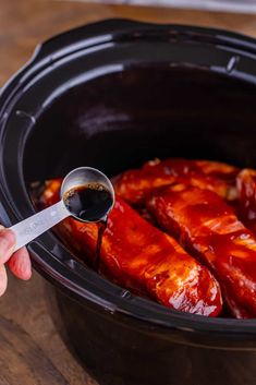 someone is spooning sauce into the slow cooker to make barbecue ribs in the crock pot