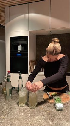 a woman in black shirt preparing food on top of a kitchen counter next to bottles