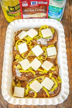 a casserole dish with cheese and onions in it on a wooden table next to two bottles of mustard