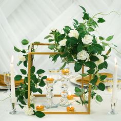 a gold frame with flowers and candles on a white table cloth covered table in a marquee