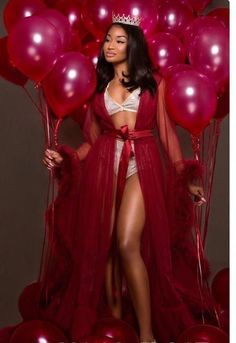 a woman wearing a red gown and crown standing in front of balloons with her hands on her hips