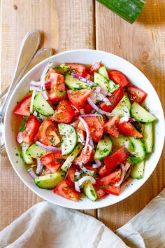 a white bowl filled with cucumber, tomatoes and onions on top of a wooden table