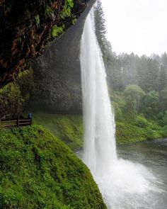 a person sitting on a bench in front of a waterfall with water falling from it