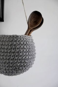 a crocheted basket hanging from a wall with a wooden spoon in it and a black frame on the wall