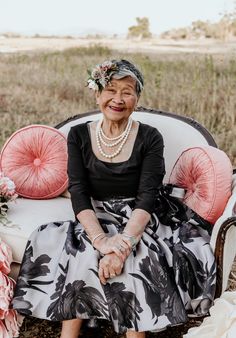 an older woman sitting on top of a white couch next to a flower filled pillow