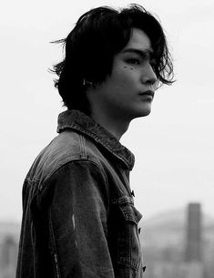 a young man with long hair standing in front of a tall building and looking off into the distance