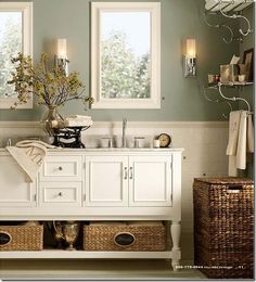 a bathroom with green walls and pictures on the wall above the vanity, along with two wicker baskets under the sink