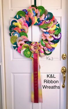 a wreath made out of paper flowers is hanging on the front door with ribbon tied around it