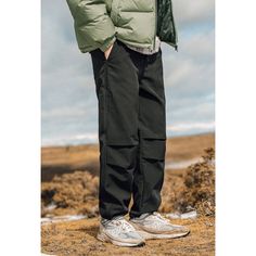 a man standing on top of a dirt field wearing a green jacket and black pants