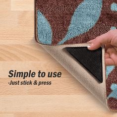 a hand touching the corner of a rug on top of a wooden floor with blue and brown designs