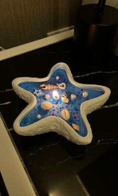 a blue and white starfish shaped candle holder on a black counter with a lamp in the background